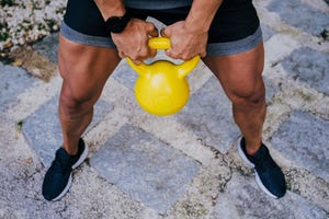 mid adult man lifting kettlebell while standing in yard