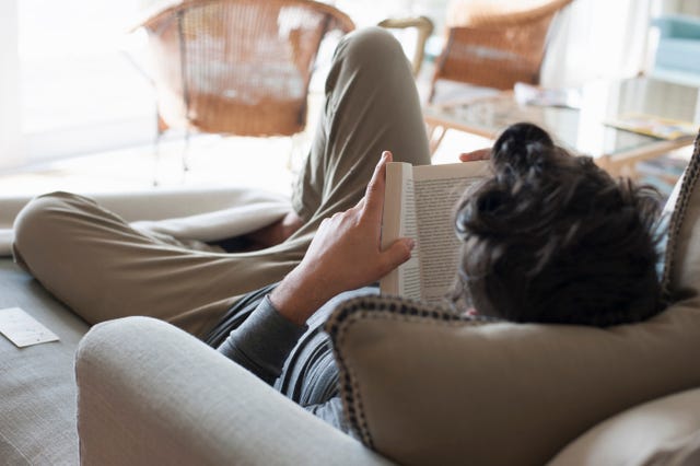 mid adult man relaxing on sofa, reading book, rear view