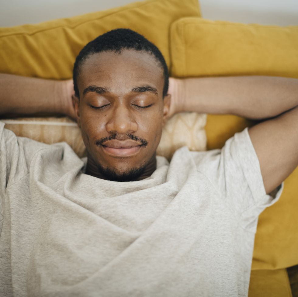 mid adult man sleeping with hands behind head on sofa in living room