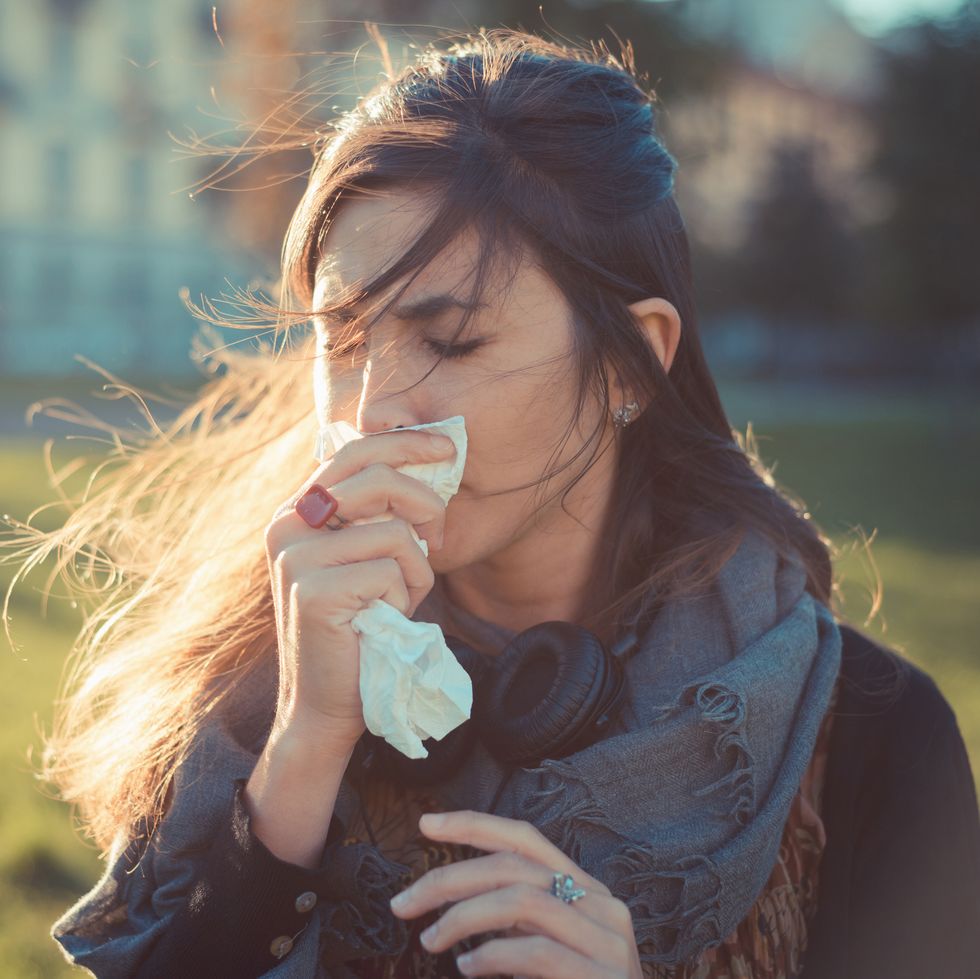 mid adult woman blowing nose with hankerchief in park