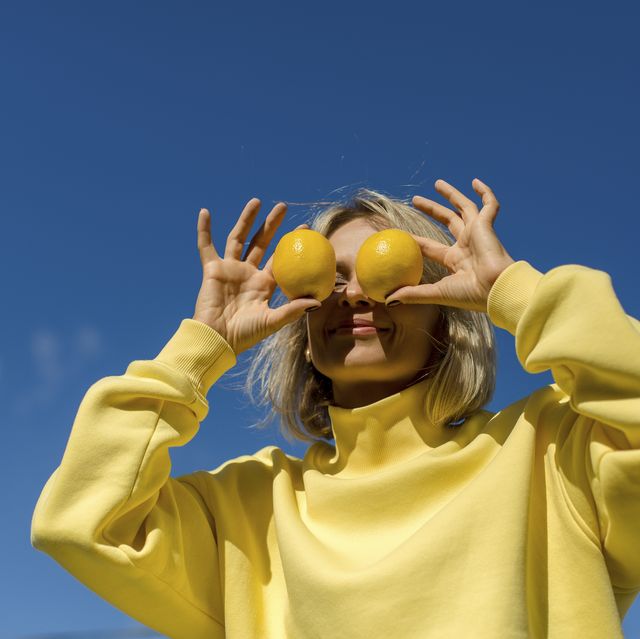 mid adult woman covering eyes with lemon during sunny day