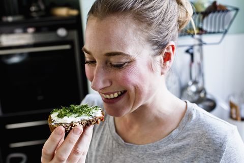 mid adult woman eating rye bread snack in kitchen