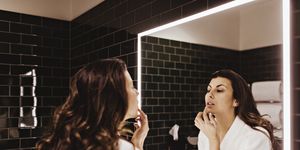mid adult woman looking in mirror while applying lip balm
