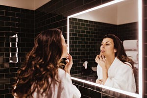 mid adult woman looking in mirror while applying lip balm