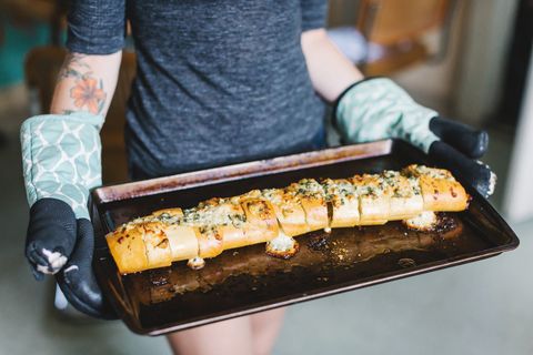 Mid section of young women holding stuffed baguette on baking tin