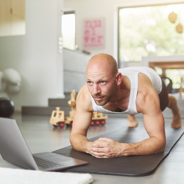 a middle aged man is exercising at home with the help of a laptop and doing fitness exercises, pushups, situps and other sporting activities on a fitness mat