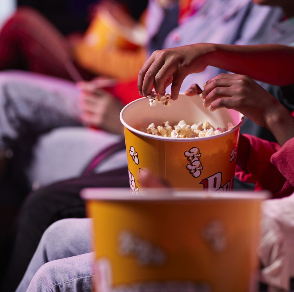 midsection of friends sharing popcorn while sitting in theater