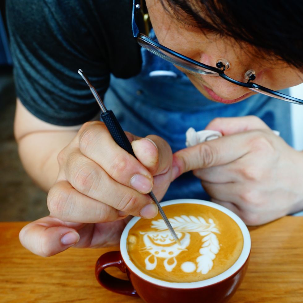 midsection of man making froth art in coffee cup on table