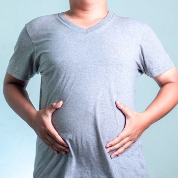 Midsection Of Man Touching Belly While Standing Against White Background