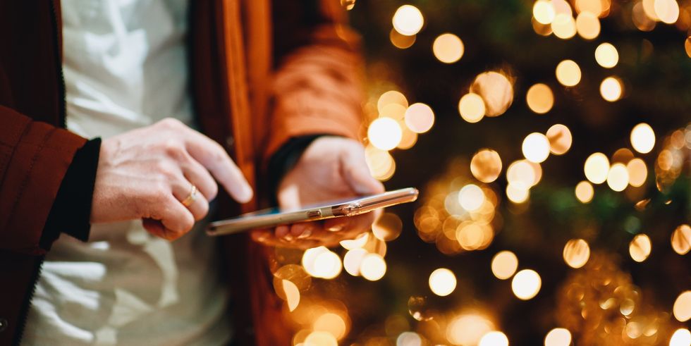 Midsection Of Man Using Smart Phone Against Illuminated Christmas Tree