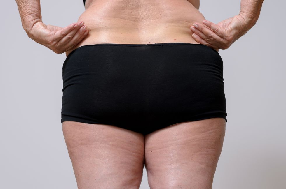 Midsection Of Overweight Senior Woman Pulling Her Waist Against Gray Background