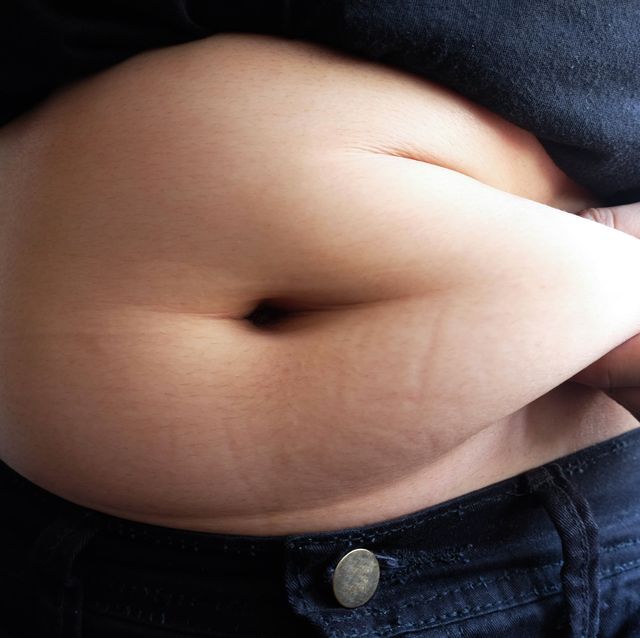 midsection of overweight woman holding stomach fats while standing against wall