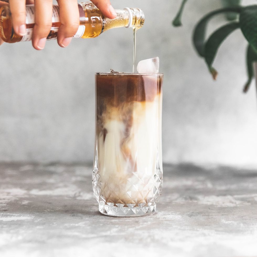 midsection of person pouring syrup into coffee in glass