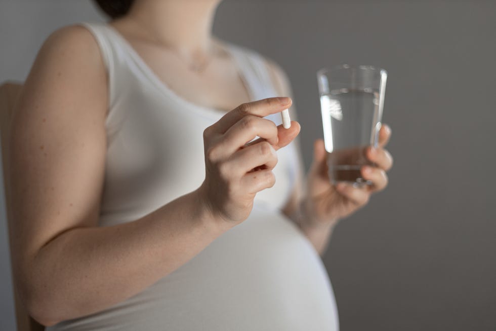 embarazada con una cápsula y un vaso de agua en la mano