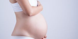 midsection of pregnant woman touching belly by gray background