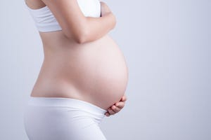 midsection of pregnant woman touching belly by gray background