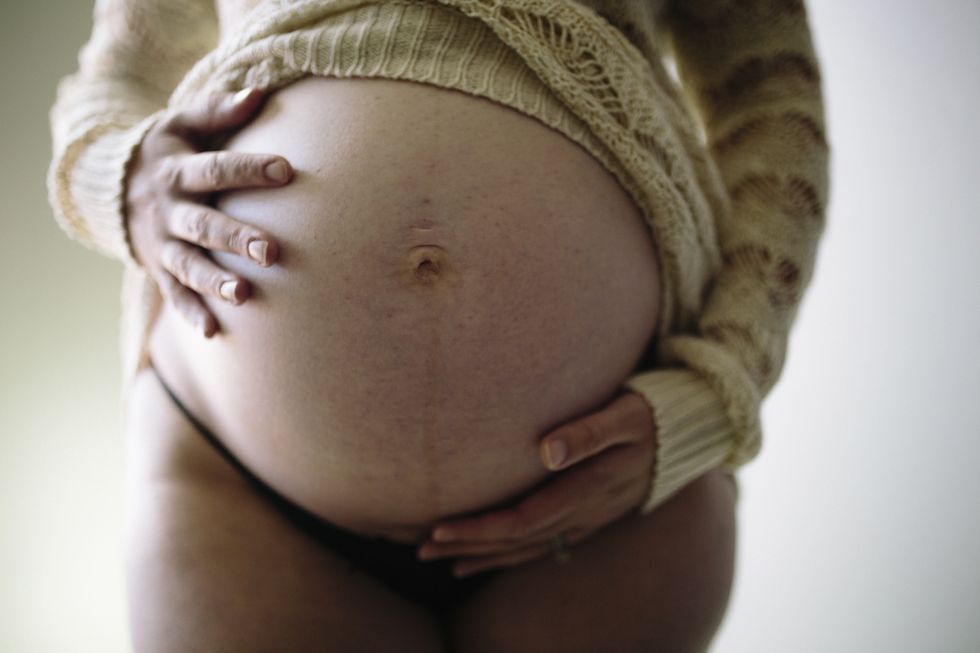 midsection of pregnant woman touching stomach while standing against wall at home