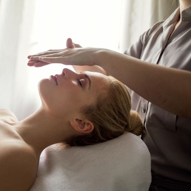 midsection of therapist giving reiki treatment to woman on face at spa