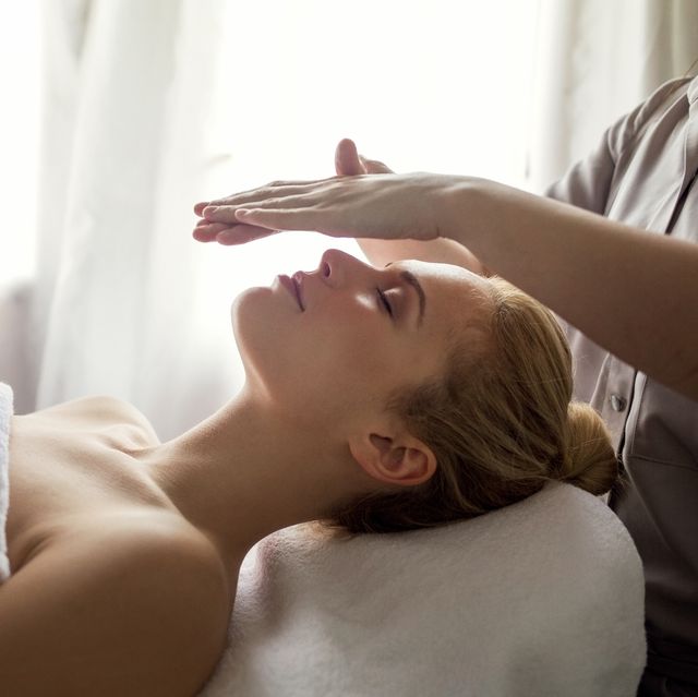 Midsection of therapist giving Reiki treatment to woman on face at spa