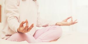 Midsection Of Woman Doing Yoga On Bed At Home