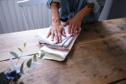 midsection of woman folding napkins while standing at wooden table in kitchen