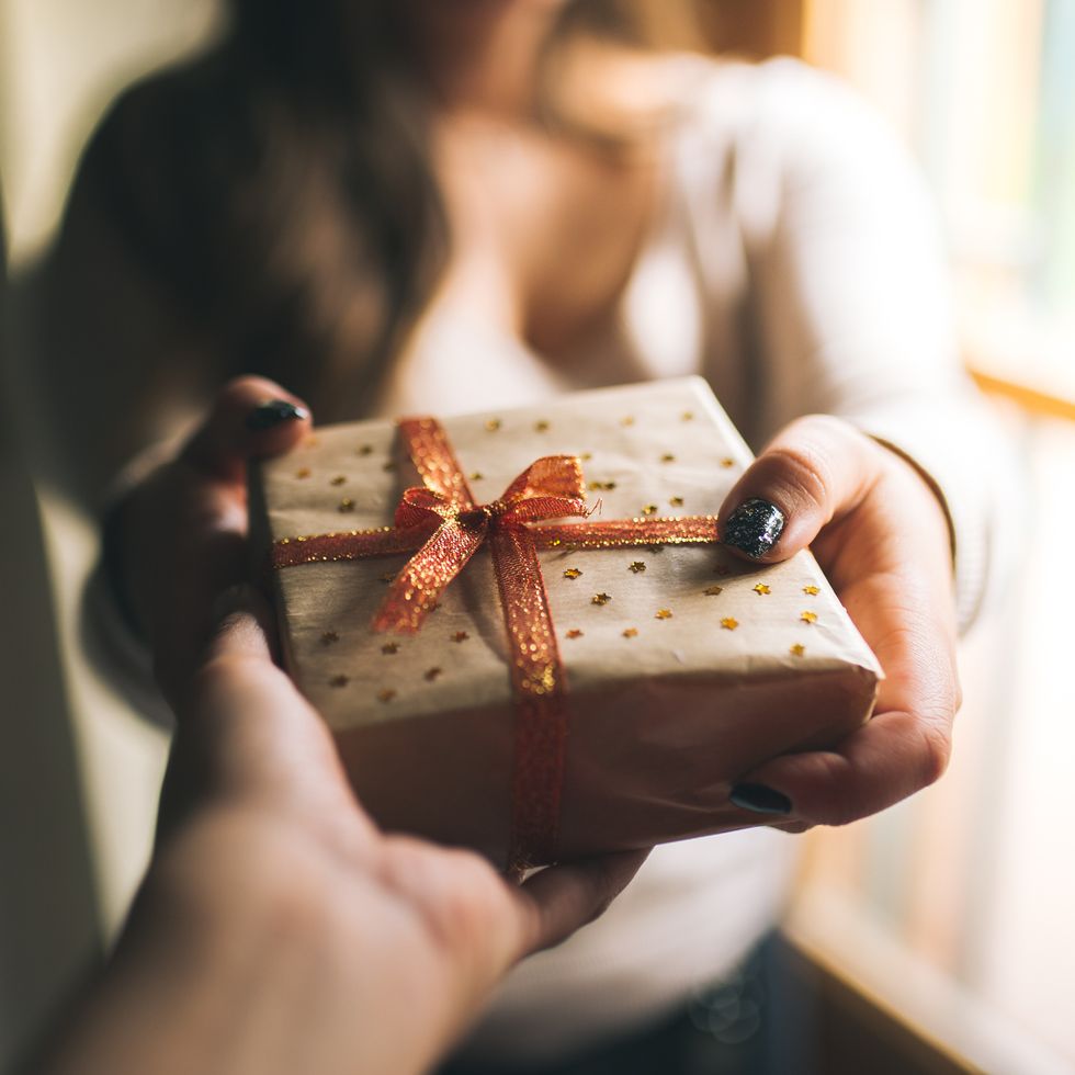 midsection of woman giving gift box to friend against window