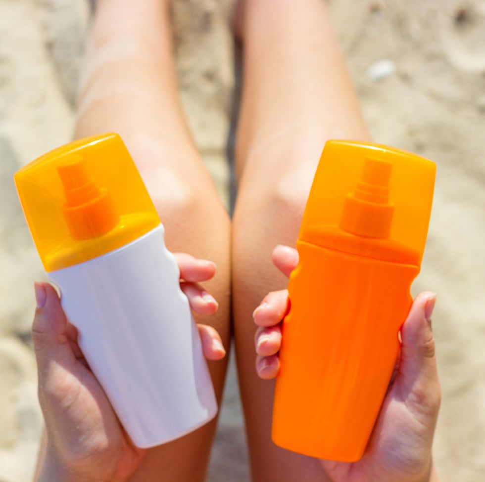 midsection of woman holding bottles while sitting on sand at beach