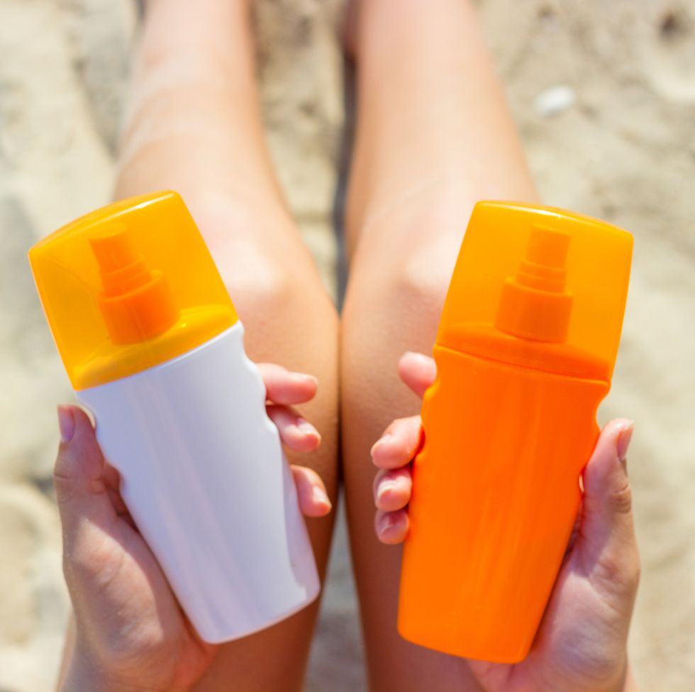 midsection of woman holding bottles while sitting on sand at beach