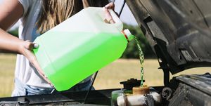 midsection of woman on road trip pouring coolant in engine during sunny day