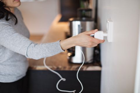 Midsection of woman plugging mobile phone charger on wall at home