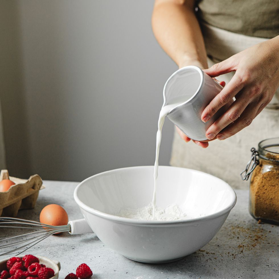 woman pouring milk on wheat flour in bowl