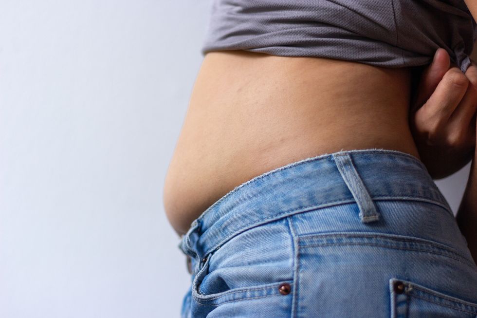 midsection of woman showing abdomen standing against wall