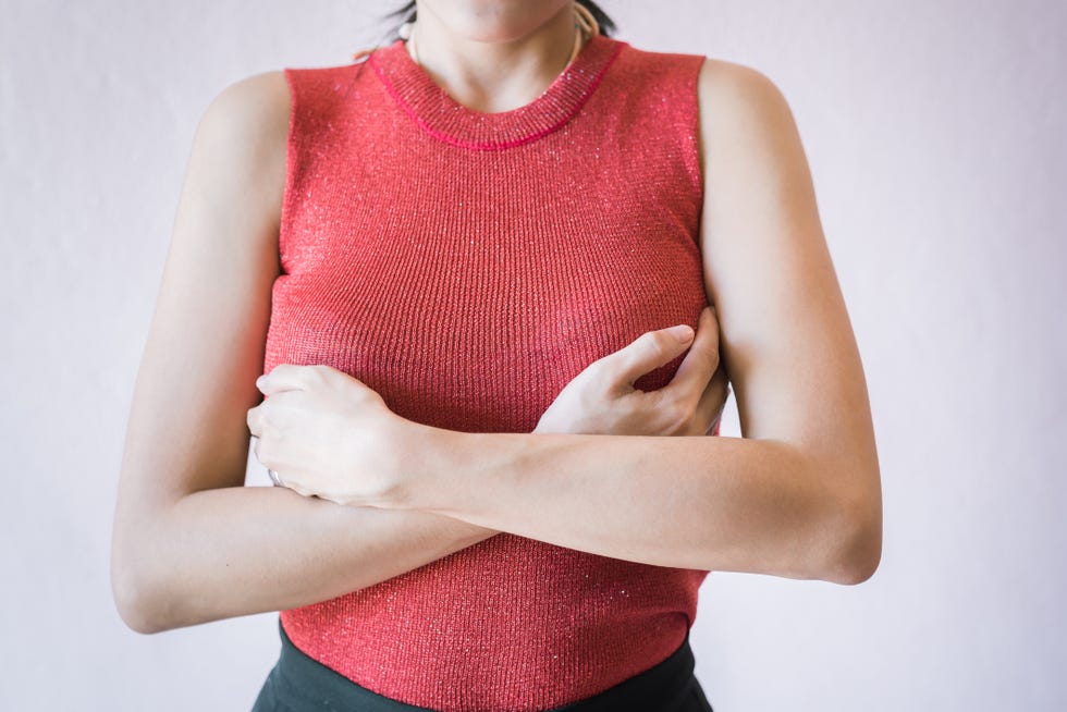 midsection of woman touching breast while suffering from cancer while standing against white background