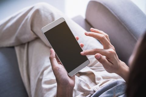 Midsection Of Woman Using Mobile Phone While Sitting On Sofa At Home