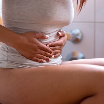 Midsection Of Woman With Hands On Stomach Sitting On Toilet Seat