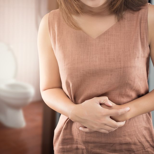 midsection of woman with stomachache standing against toilet