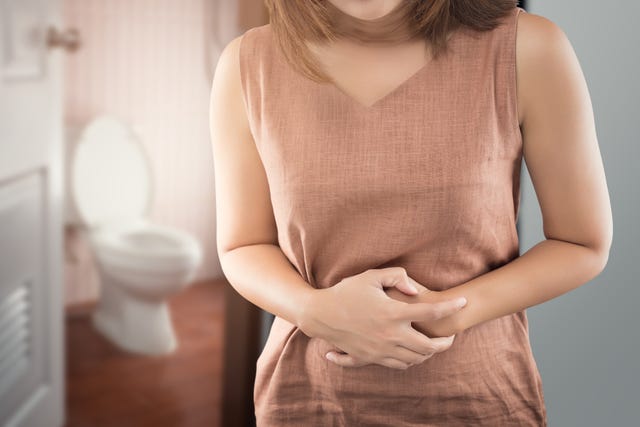 midsection of woman with stomachache standing against toilet