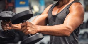 Midsection Of Young Man Lifting Dumbbell In Gym