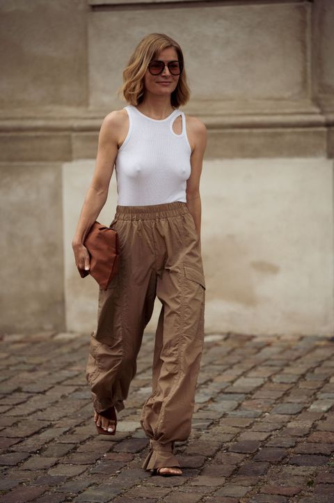 a woman wearing a cute out white tank, light brown cargo pants, a brown leather clutch, and heels during copenhagen fashion week in a roundup of cute summer outfits 2023