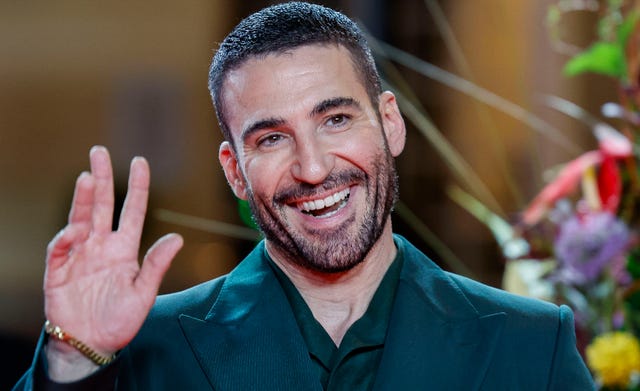 miguel angel silvestre sonriendo y saludando con una mano