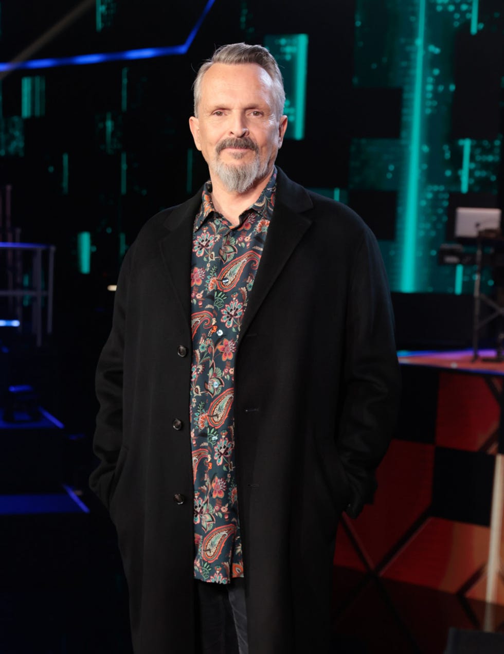 el cantante con abrigo negro y camisa estampada