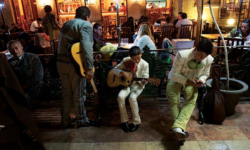 In de Jardn de la Unin van Guanajuato tokkelt een jonge mariachi op zijn gitaar terwijl zijn opa hun volgende optreden voorbereidt
