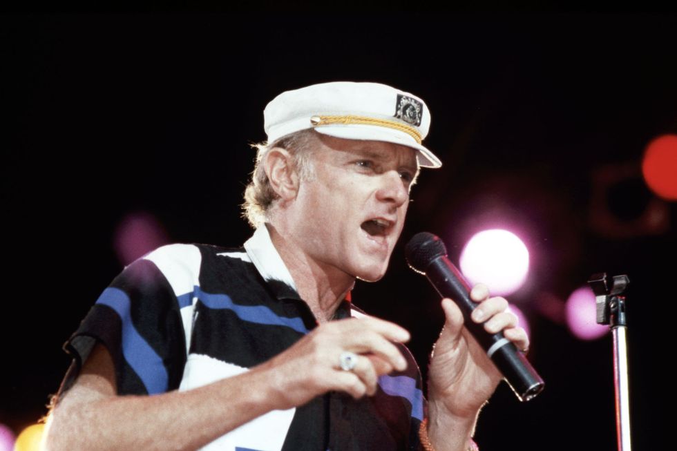man wearing a yacht captain hat and singing into a microphone on stage