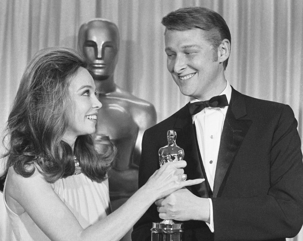 mike nichols, right, is wearing a suit and smiling as he accepts an oscar for best director from a woman standing on the left