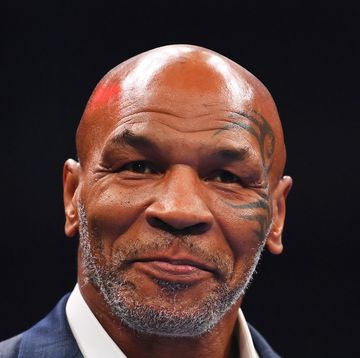 boxing champion mike tyson smiles and looks past the camera, he wears a blue suit jacket and white collared shirt