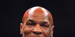 boxing champion mike tyson smiles and looks past the camera, he wears a blue suit jacket and white collared shirt