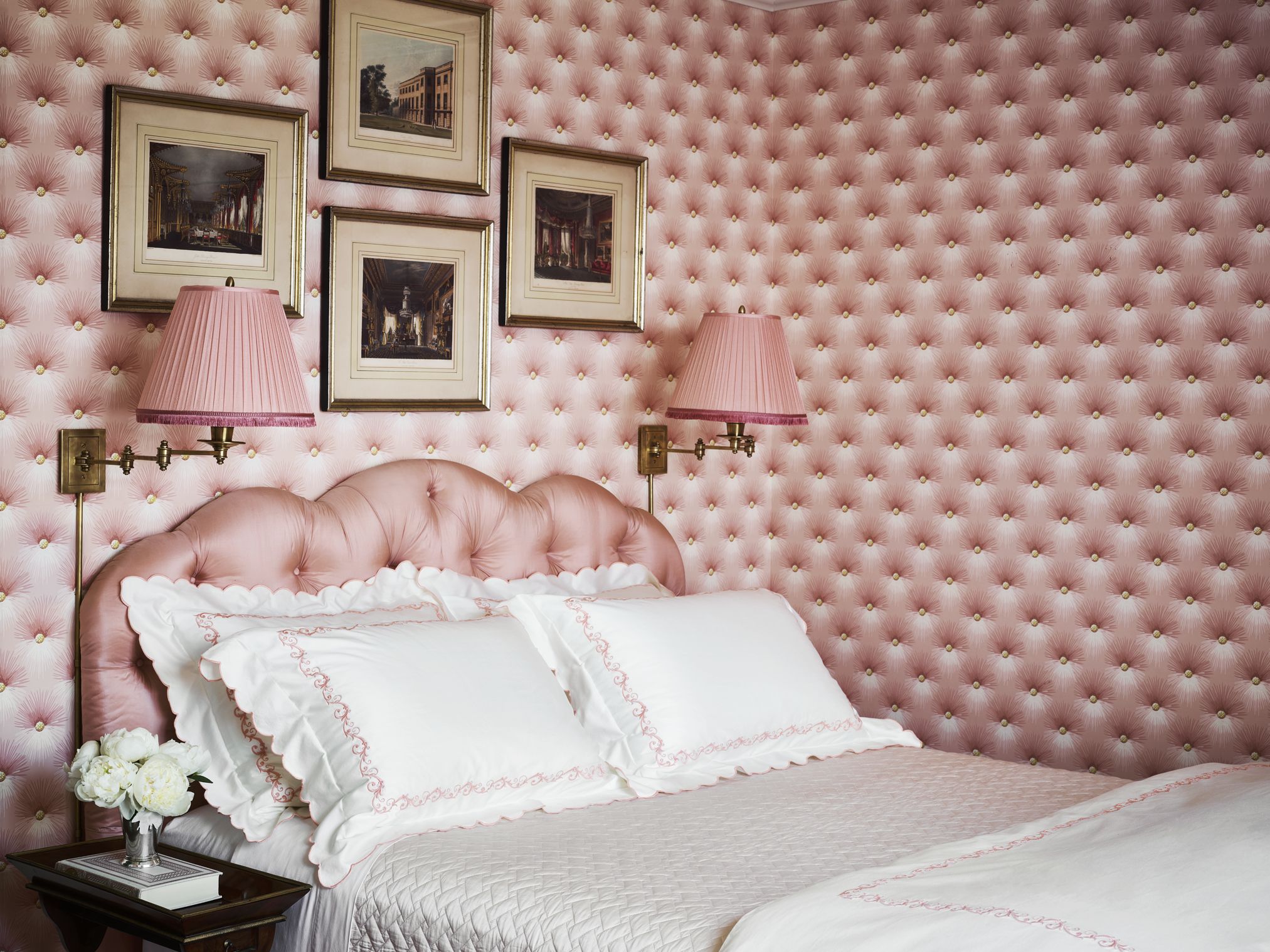 a pink upholstered headboard and white bedding against a pink and white patterned wallpaper