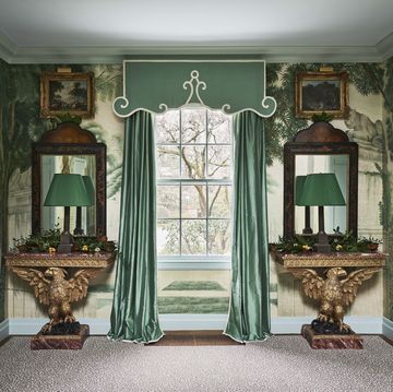 a window is framed by green silk curtains with large eagle based tables on either side with mirrors and lamps