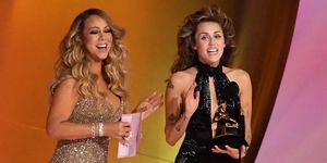 miley cyrus giving a speech at the grammys as mariah carey smiles after giving her an award