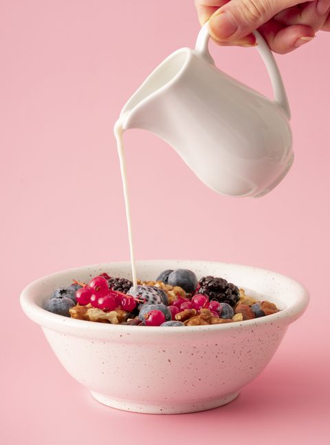 milk poured on bowl of granola and berries on pink background
